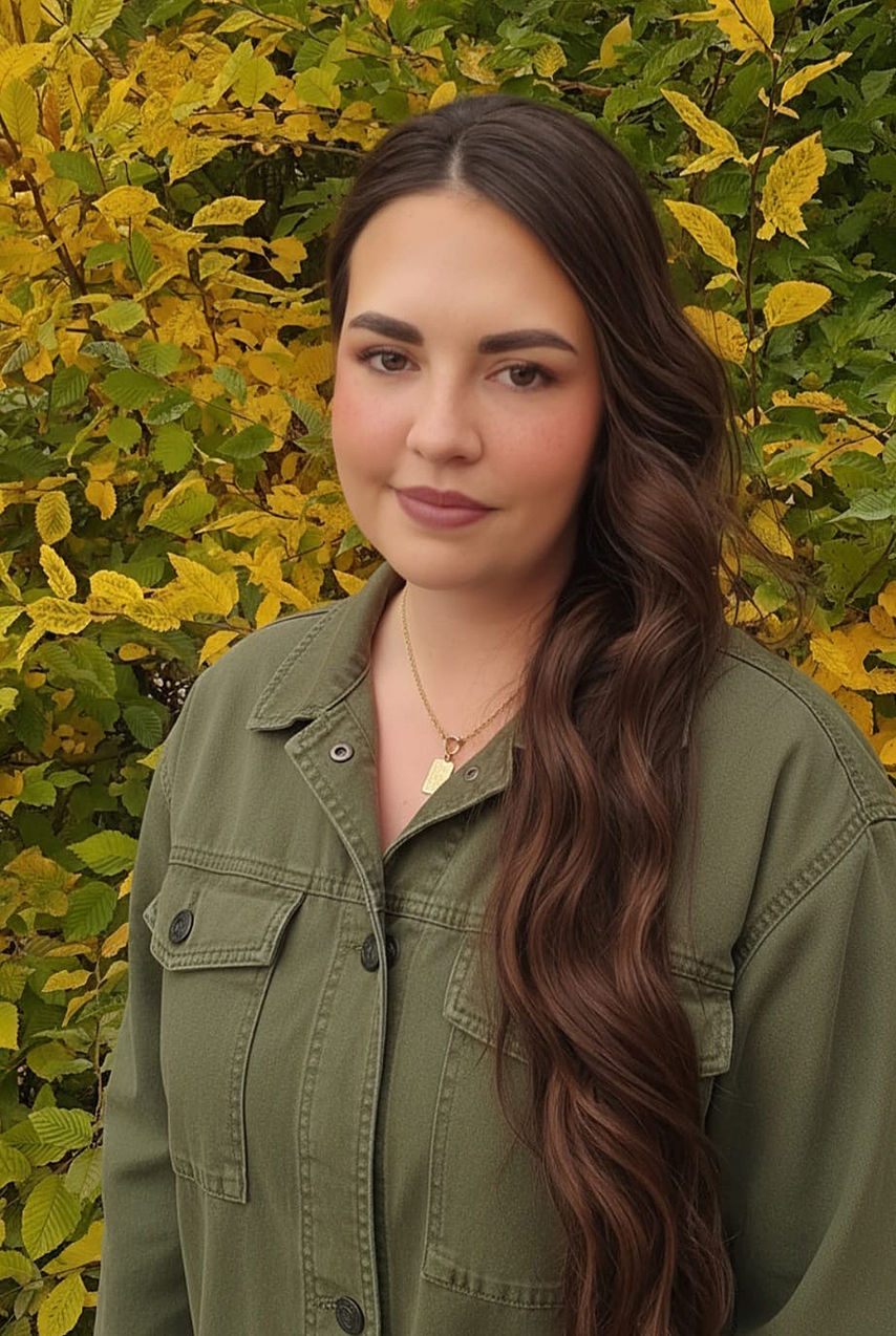 Frau mit sehr langen braunen Haaren, stehend vor grünem Strauch, Oberkörper sichtbar, Porträt im Freien